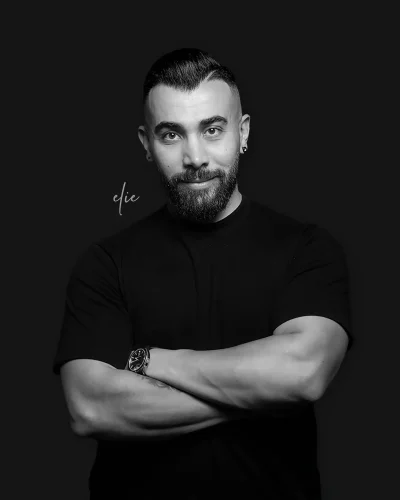Black and white studio portrait of a UX UI designer with arms crossed on a dark background.
